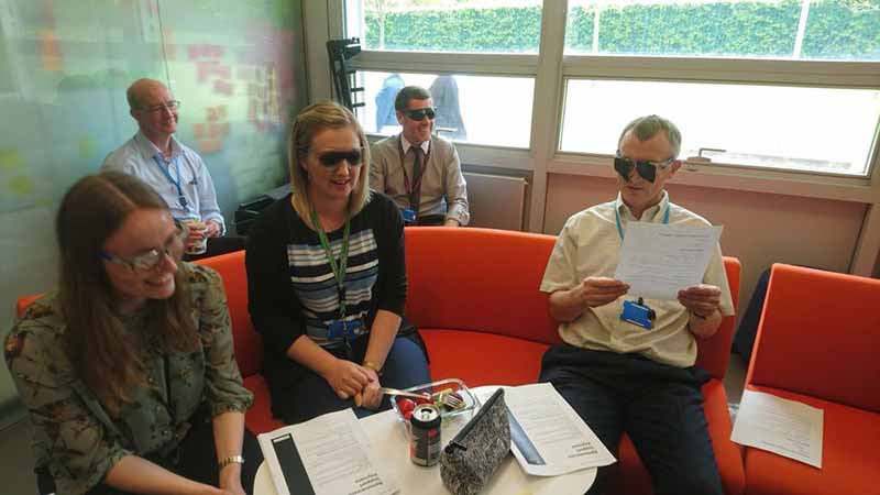 A group of people wearing simulation glasses holding paper forms